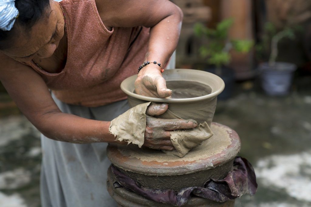 asian woman working on shaping a bowl on a pottery wheel