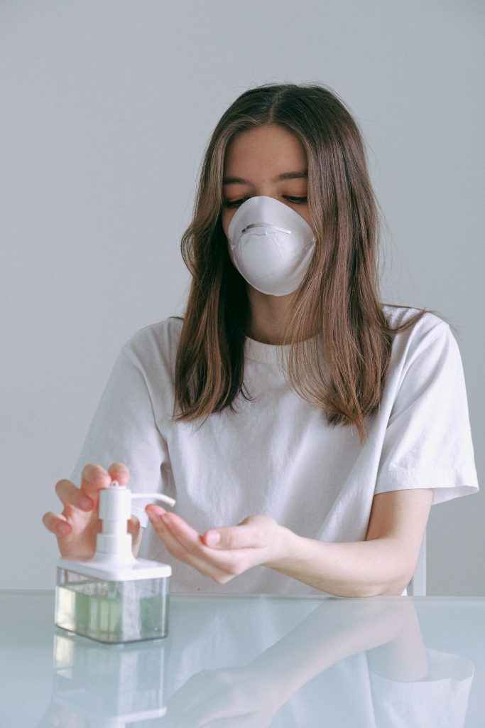 woman in white shirt with facemask applying hand sanitizer